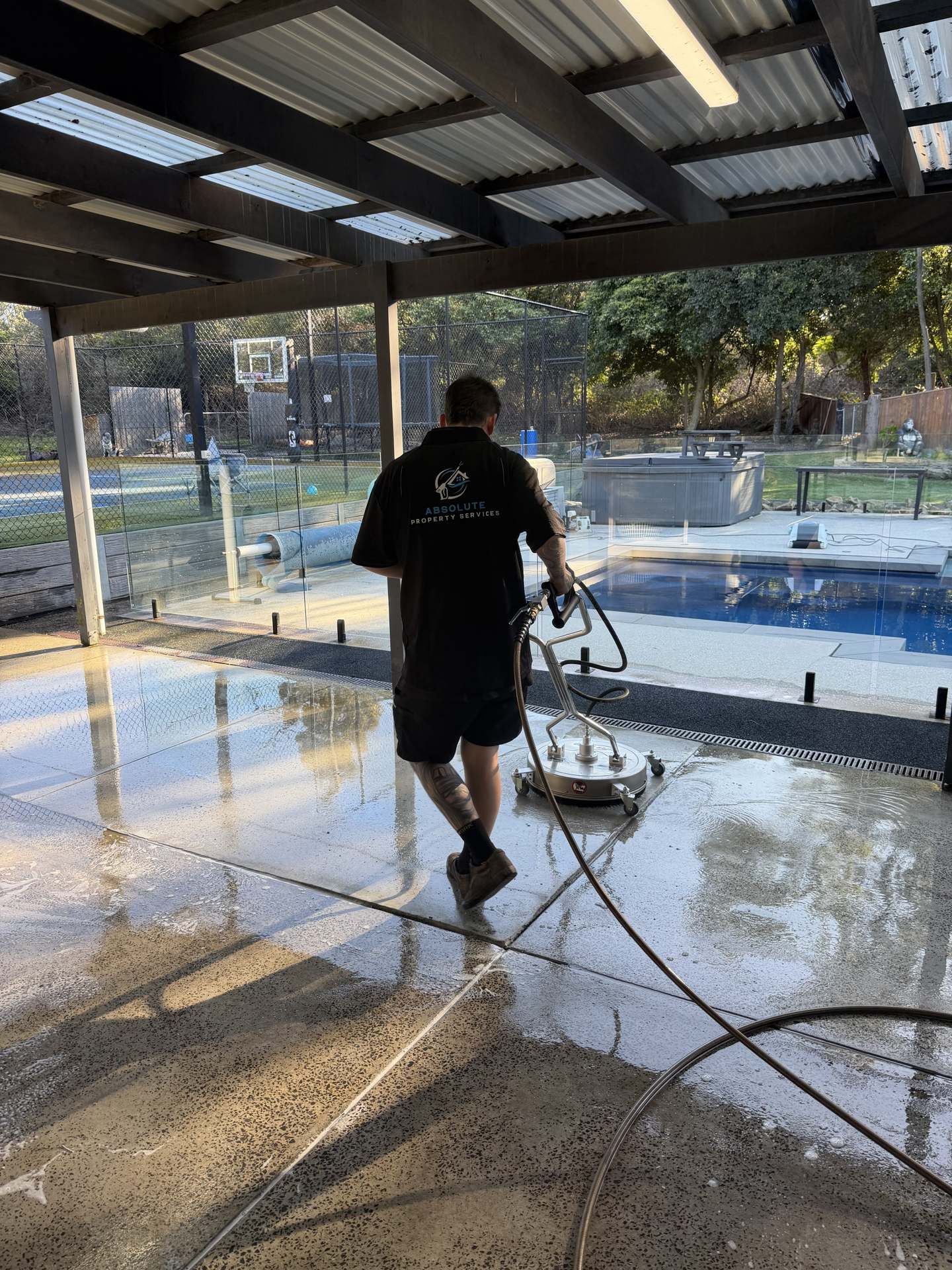 Absolute Property Services technician pressure washing a pool patio